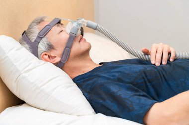 Orta yaşlı Asyalı adam uyurken Cpap başlık takıyor.