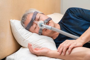 Orta yaşlı Asyalı adam uyurken Cpap başlık takıyor.