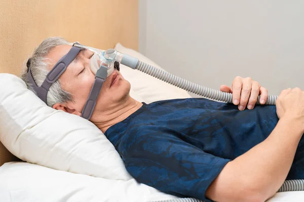 Orta yaşlı Asyalı adam uyurken Cpap başlık takıyor.