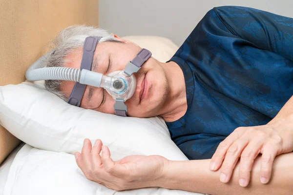 Idade Média Homem asiático vestindo capacete CPAP durante o sono — Fotografia de Stock