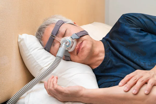 Orta yaşlı Asyalı adam uyurken Cpap başlık takıyor.