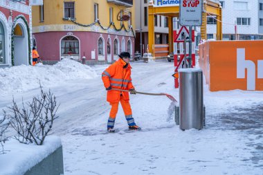 Road cleanup worker in bright orange coat clearing up snow from 