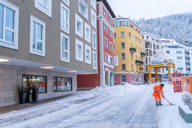 Road cleanup worker in bright orange coat clearing up snow from 