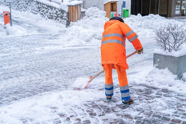 Road cleanup worker in bright orange coat clearing up snow from 