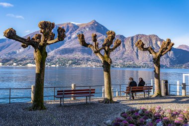 İnsanlar banklarda oturur ve İtalya, Varenna 'daki Como Gölü' nün güzel manzarasının tadını çıkarırlar.
