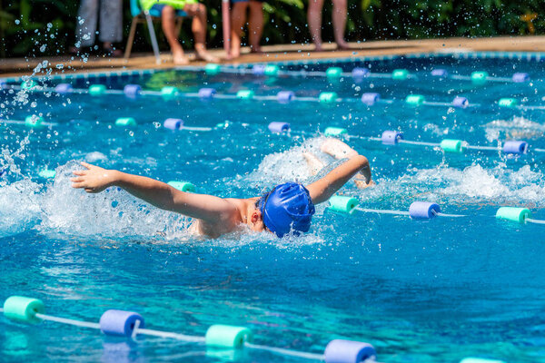 Young boy swimmer doing butterfly stroke at a pool on a bright sunny day