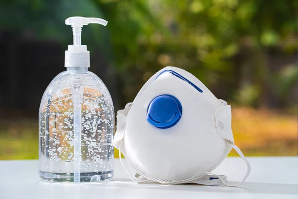 Antiseptik el jeli ve N95 maskesi, COVID-19 veya corona virüsünden korumak için beyaz masa ve bulanık bahçe arka planı, sağlık konsepti