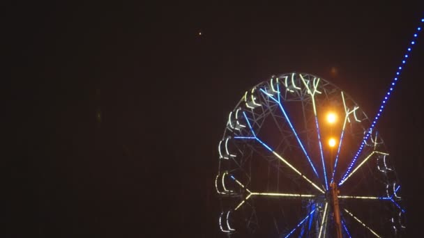 Колесо обозрения вращается в парке развлечений под темным ночным небом — стоковое видео