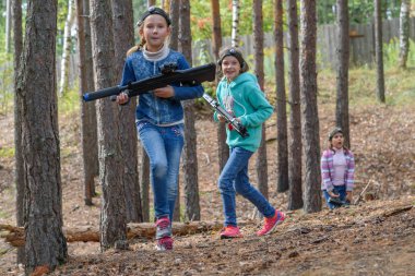 Lazer tabancalı iki kız ormanda koşuyor. Lazer savaşı, kızılötesi ışınları ateşleyen silahlarla oynanan bir oyun. Geniş yaşlar için popüler bir oyun. Sınıf arkadaşları dışarıda birlikte oynarlar.