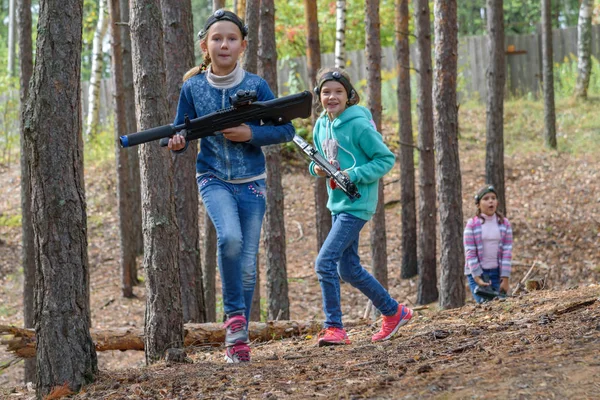 两个拿着激光手枪的女孩正在森林里奔跑。 激光标签，一个用枪射击红外光束的游戏。 一种广受欢迎的年龄游戏。 同学们一起在户外玩耍 — 图库照片