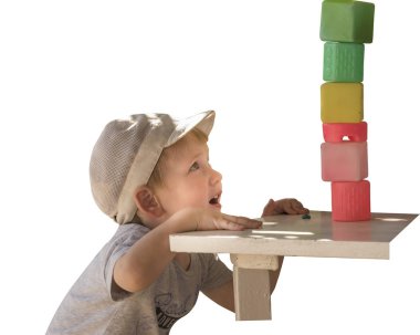 A little boy plays with colored cubes, builds a pyramid. Isolated