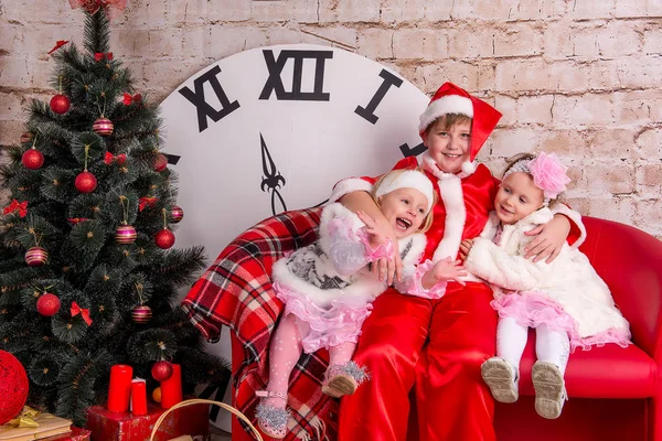 The children, a boy dressed as Santa Claus and two girls in white coats posing against the backdrop of the Christmas decorations in the studio.