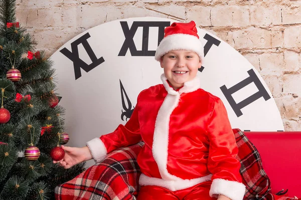 Die Kinder, ein als Weihnachtsmann verkleideter Junge posiert auf dem Hintergrund des Weihnachtsbaums. — Stockfoto