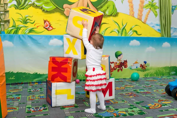 Liten flicka spelar i underhållning med färgade kuber som visar bokstäverna i alfabetet. — Stockfoto