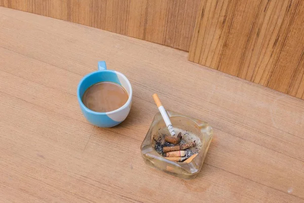 コーヒーと灰皿、ソフト フォーカスの木製テーブルで燃えているタバコ — ストック写真