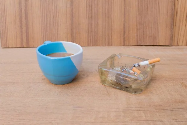 Coffee and burning cigarette in ashtray,soft-focus wooden table — Stock Photo, Image