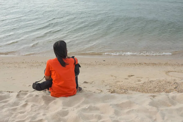 Jovem mulher sentada na praia e olha para o mar — Fotografia de Stock