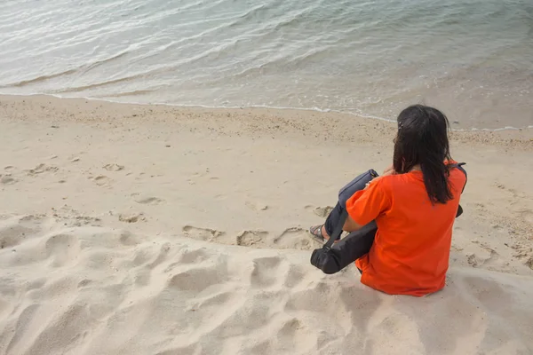 Jovem mulher sentada na praia e olha para o mar — Fotografia de Stock