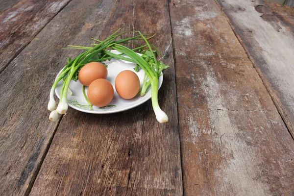 Свіже куряче яйце на тарілці крупним планом і цибулею в дерев'яному столі — стокове фото
