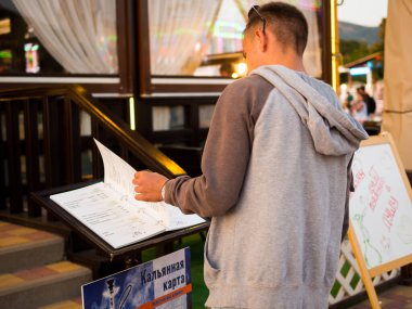 Kabardinka, Rusya - 8 Ağustos 2019: Bir adam sokakta bir kafenin girişindeki menüyü okuyor