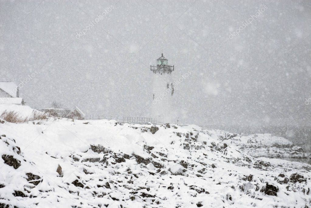 Lighthouse in Snowstorm by Rocky Coast in New England