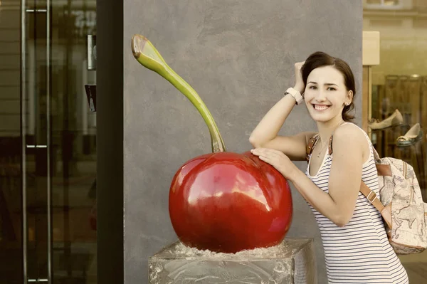 Büyük yapay kiraz yaslanmış bir sırt çantası ile güzel kız