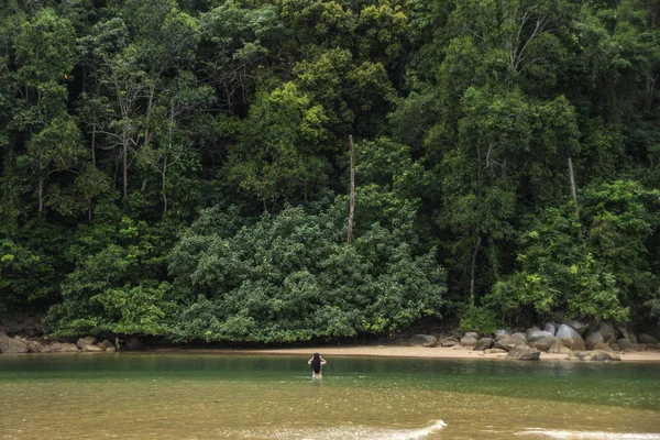 La chica se para en el agua frente a la enorme colina cubierta de árboles — Foto de Stock
