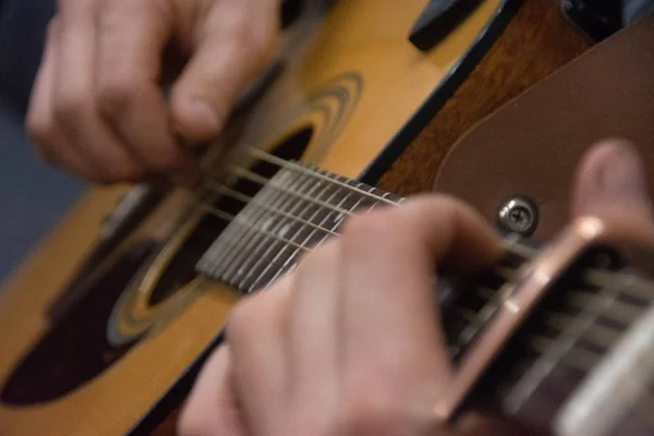 Gitarrendeck und Gitarrist reichen sich die Hände. Capo auf dem Griffbrett einer Gitarre. Unscharfer Gitarrenhintergrund — Stockfoto