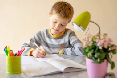 Çocuk ev ödevini yapıyor. Çocuk uzaktan öğreniyor işte. Bir çocuk masaya oturur ve yazar. Çevrim içi öğrenim