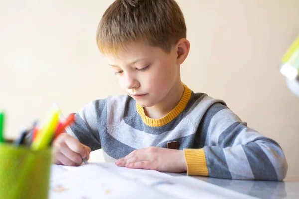 Il ragazzo fa i compiti. Il bambino sta imparando a distanza. Un ragazzo si siede a un tavolo e scrive. Apprendimento online — Foto Stock