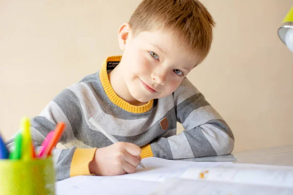 Çocuk ev ödevini yapıyor. Çocuk uzaktan öğreniyor işte. Bir çocuk masaya oturur ve yazar. Çevrim içi öğrenim