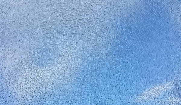 Vatten droppar på glaset med suddiga blå himmel bakgrund — Stockfoto