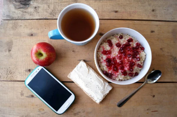 Healthy breakfast, vegetarian. Oatmeal with cranberries, apple, sandwich with cream cheese, tea, mobile phone. — Stock Photo, Image