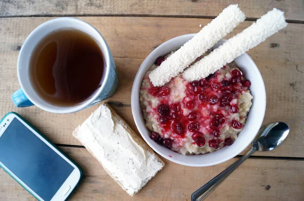 Pequeno-almoço saudável, vegetariano. Farinha de aveia com cranberries, sanduíche com creme de queijo, paus de coco, chá, telefone móvel . — Fotografia de Stock