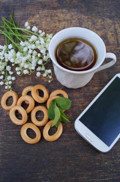 喝杯茶木制的桌子用款手机用一个空白的屏幕上和花香 免版税图库照片