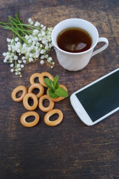 喝杯茶木制的桌子用款手机用一个空白的屏幕上和花香 免版税图库图片