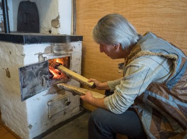 Yetişkin bir adam evin sıcak olmasını için yakacak odun huş ocakla yangında fueling bir kürk umut içinde