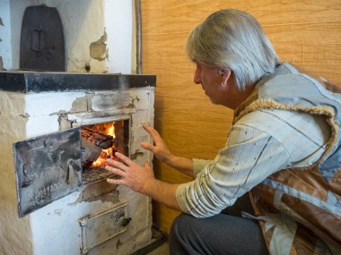 Ellerini ısınma ve nerede yanan odun huş ağacı soba ateşe bakarak bir kürk yelek yetişkin bir erkekte