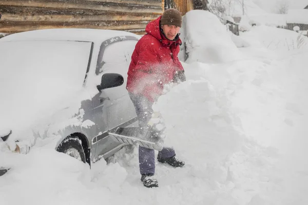 man in red jacket cleans black shovel snow near his car because it snowed a lot