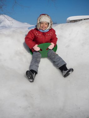 Kırmızı ceketli bir slayt yeşil buz pateni pisti üzerinde sürme mutlu kız