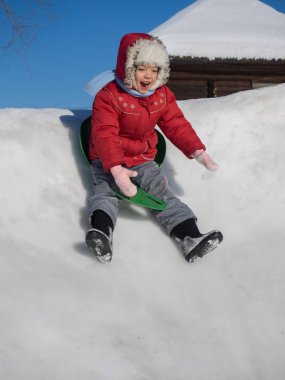 Kırmızı ceketli bir slayt yeşil buz pateni pisti üzerinde sürme mutlu kız