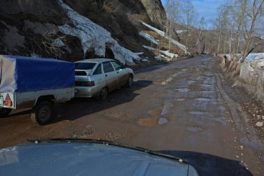 çukurlar ve yolcu araba gri mavi bir tente ile kapalı römork ile binmek için su birikintileri kırık yol