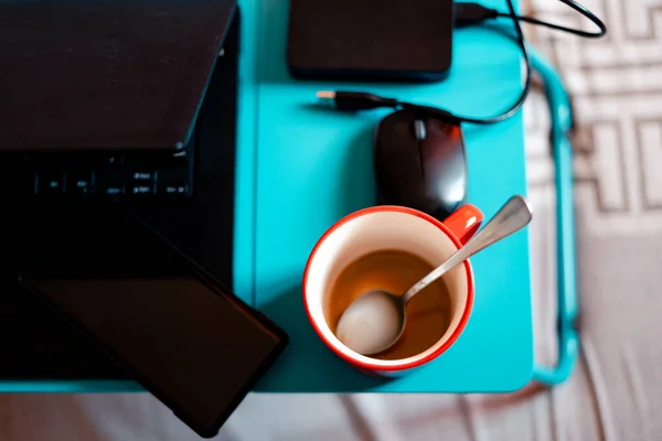 Work from home workspace set-up during Coronavirus pandemic. Red mug, laptop competer,portable hard disk and lap desk.