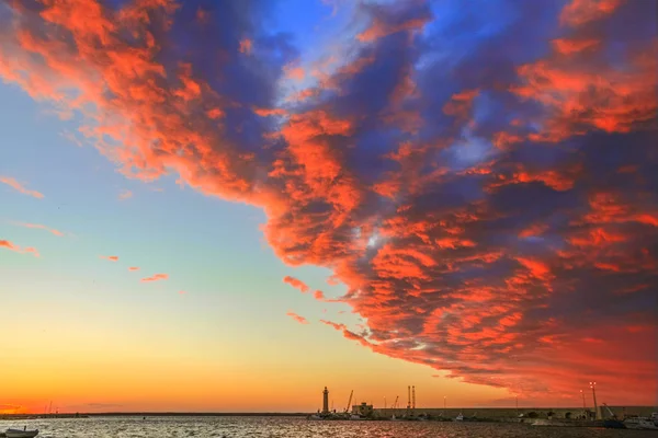 Molfetta barátait harbour uralta narancsszínű felhők napnyugtakor: a háttérben a világítótorony és a móló. Apulia, Olaszország. — Stock Fotó