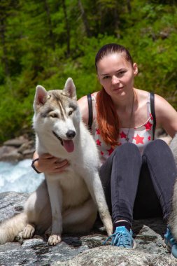 Kahverengi saçlı ve beyaz kazaklı genç bir kadın göl kenarındaki rıhtımda sakin suyla oturuyor. Sibiryalı iri yarı bir dişi köpek kızın yanında uzanıyor. Arkadaki Alpler dağları.