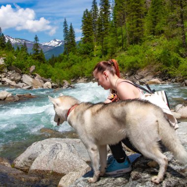 Kahverengi saçlı ve beyaz kazaklı genç bir kadın göl kenarındaki rıhtımda sakin suyla oturuyor. Sibiryalı iri yarı bir dişi köpek kızın yanında uzanıyor. Arkadaki Alpler dağları.