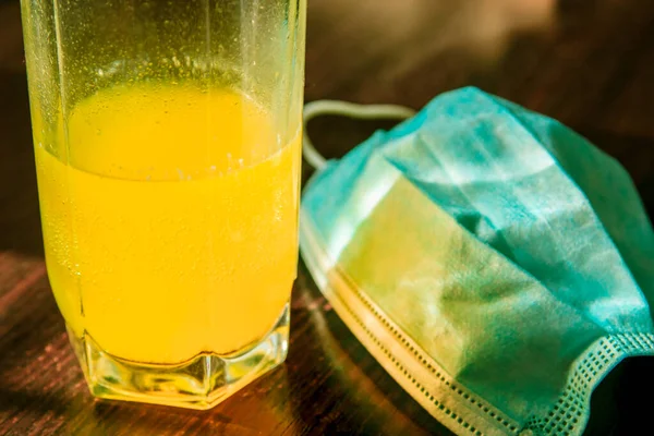 Glass of fizzy yellow vitamins drink near the medical blue mask. Illness prevention and health care concept