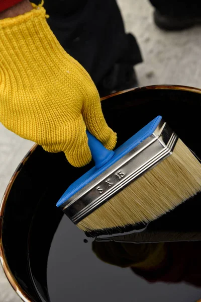 Roofers hand in yellow mittens holding a brush — Stock Photo, Image