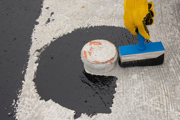 Работник наносит битумную мастику на фундамент