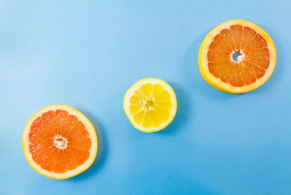 One lemon and two grapefruit slices on blue background